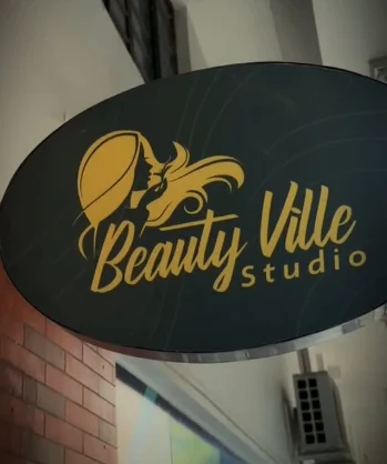 Letreiro oval com o logotipo dourado da Beauty Ville Studio na entrada do salão