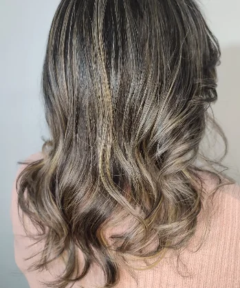 Morena iluminada com mechas finas douradas e pontas onduladas